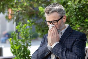 Picture of an older man sneezing into a tissue due to allergies.