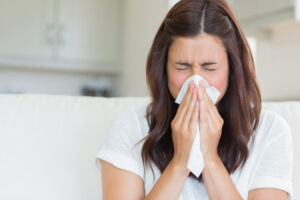 Picture of a woman sneezing into a tissue.